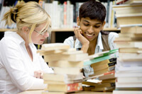 Two students studying in a library surrounded by books