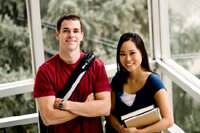 Male student in red t-shirt standing with female student in blue t-shirt hold books. Both are smiling