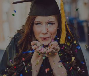 Graduated student in cap and gown blowing glitter at the camera