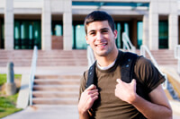 Smiling student in a brown t-shirt wearing a backpack in front of a white university building