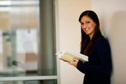 Smiling woman in a black sweater leaning against a wall and holding a book