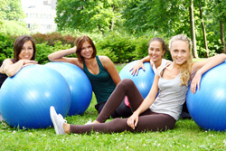 Four women sitting on grass. Each has a blue yoga ball