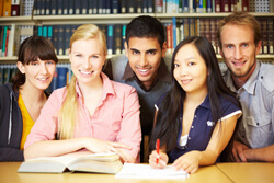 five students smiling and looking at the camera in a library