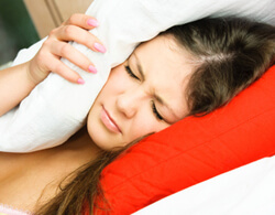 Girl with her eyes closed and face scrunched in pain laying in bed with a pillow over her head