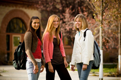 Three female students in jackets standing and smiling outside their university